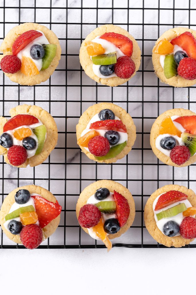 Fruit pizza cookie cups on a bakers rack with colorful fruit and creamy filling.