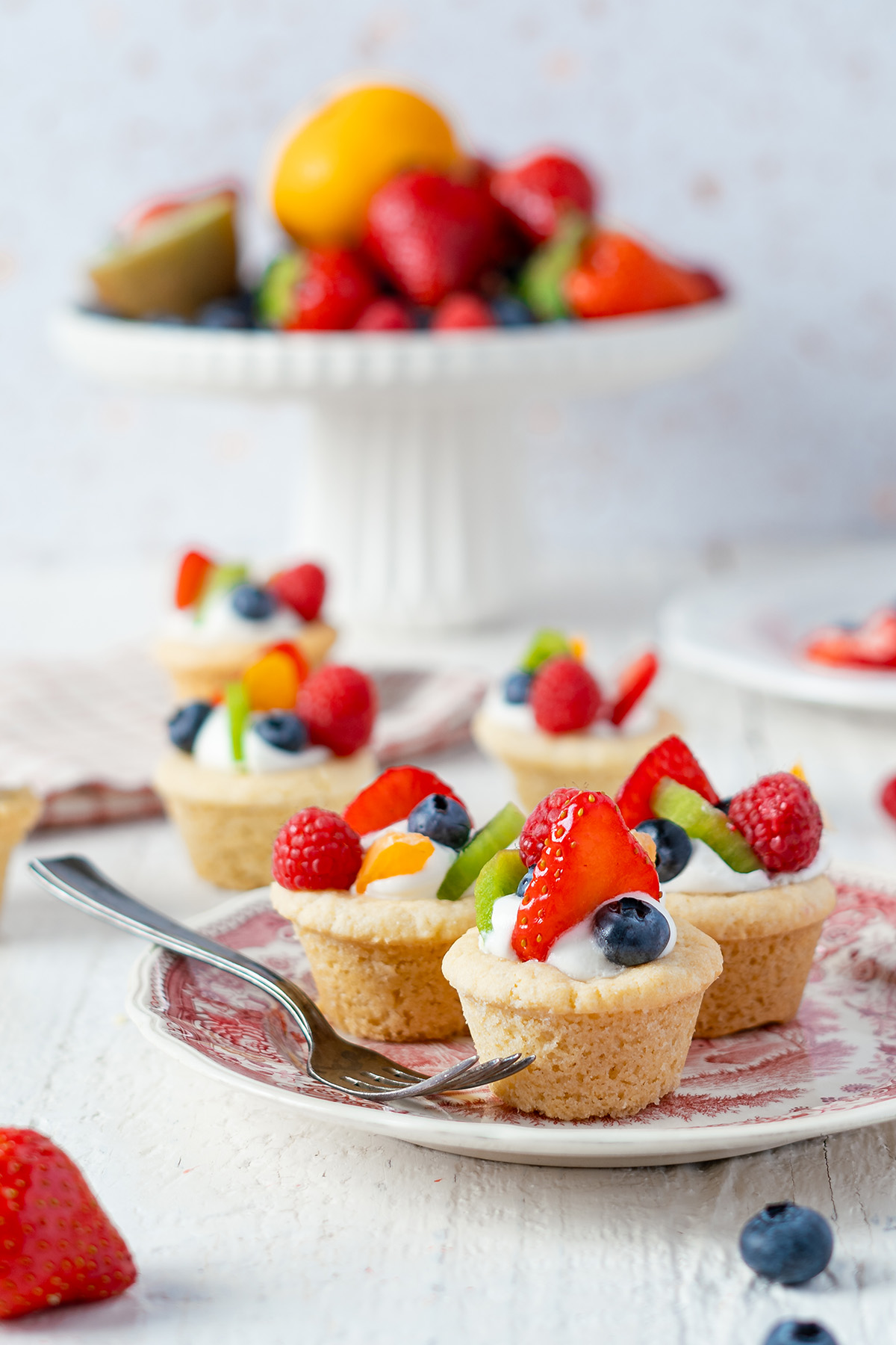 Platter of fruit pizza cookie cups topped with berries, kiwi, and oranges.