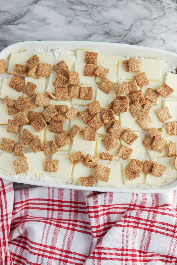 Cinnamon Toast Crunch cereal sprinkled over the butter and cake mix layers in the baking dish.