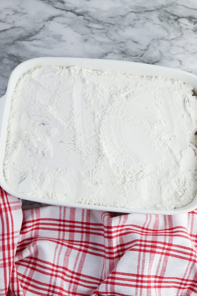 Dry yellow cake mix sprinkled evenly over the apple pie filling in a baking dish.