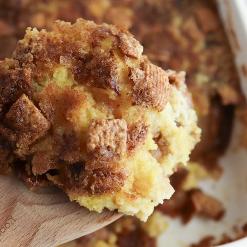Warm Cinnamon Toast Crunch apple dump cake being served from a baking dish on a wooden spoon.