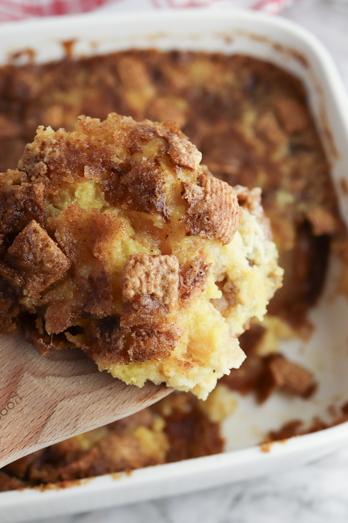 Warm Cinnamon Toast Crunch apple dump cake being served from a baking dish on a wooden spoon.